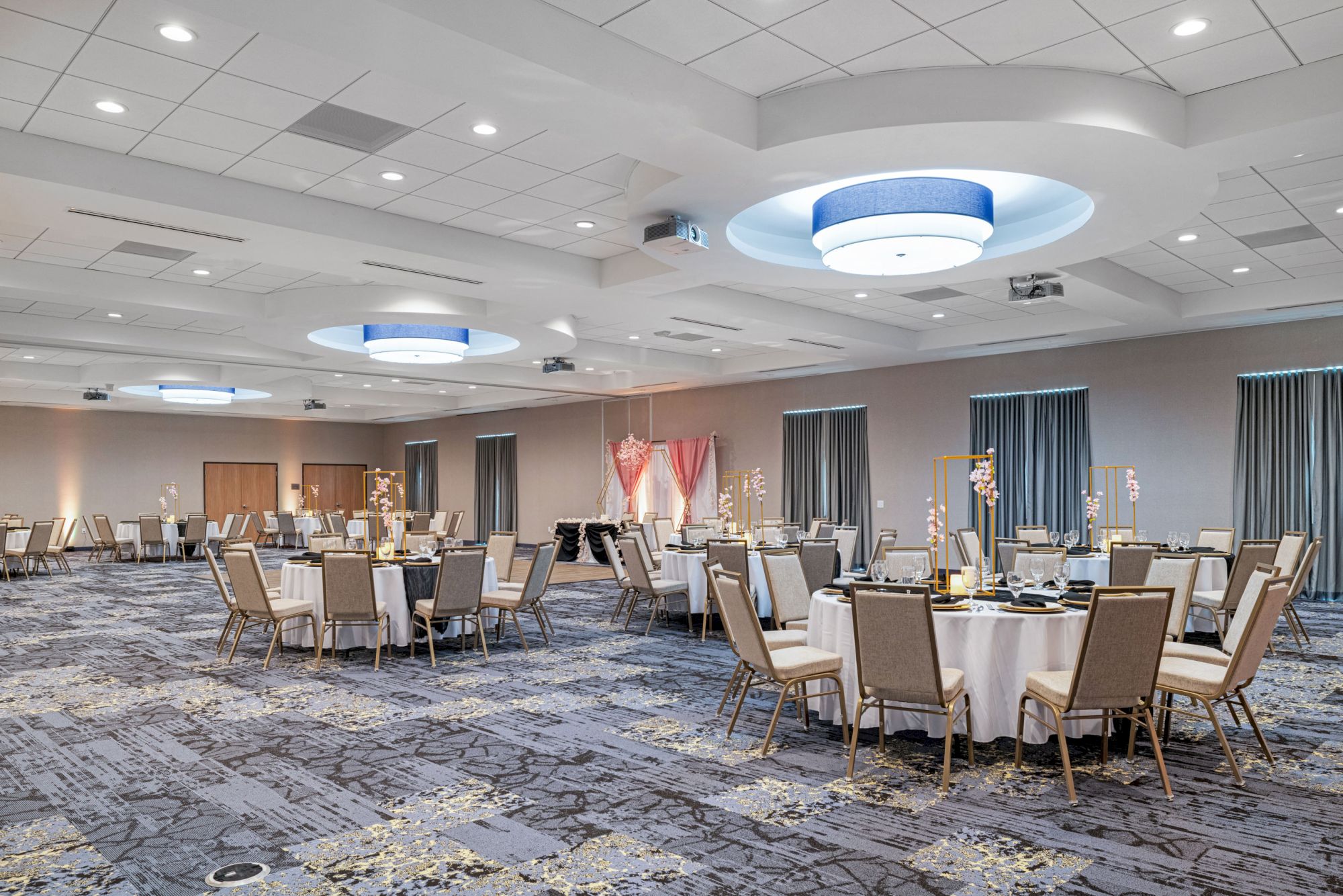This image shows a large, elegant banquet hall set up with round tables and chairs, with subtle decorations and dimmed ceiling lights giving a serene ambiance.