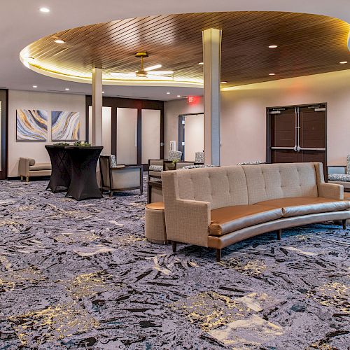 A modern, spacious lobby with carpet flooring, contemporary seating, and ambient lighting. Stylish decor and artwork adorn the walls.
