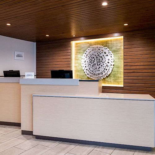 A modern reception desk area with two counters, a wooden ceiling, and a decorative wall art piece behind. The space looks clean and minimalist.