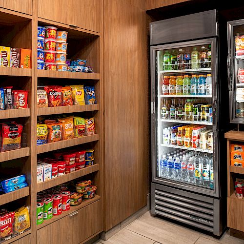 The image shows a small convenience store with shelves and a refrigerated section stocked with snacks, beverages, and various packaged goods ending the sentence.