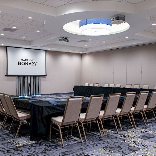 This image shows a conference room with arranged chairs, a projector screen, and a 'Marriott Bonvoy' logo on the screen.