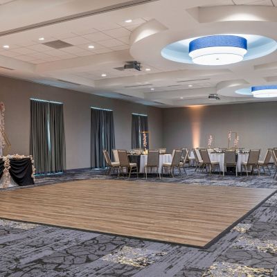 An elegantly decorated event hall with round tables and chiavari chairs set up, featuring a dance floor and lighting, ready for a special occasion.