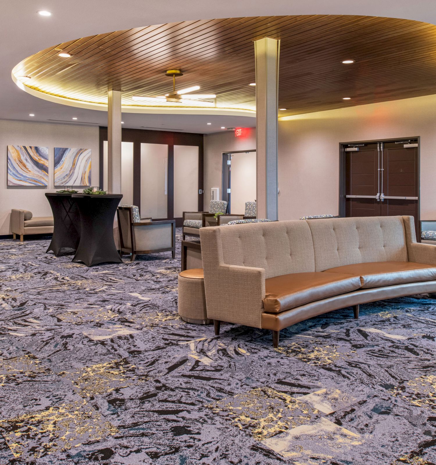 A modern lounge area with stylish furniture, decorative lighting, abstract artwork, and blue patterned carpet, creating a welcoming atmosphere.