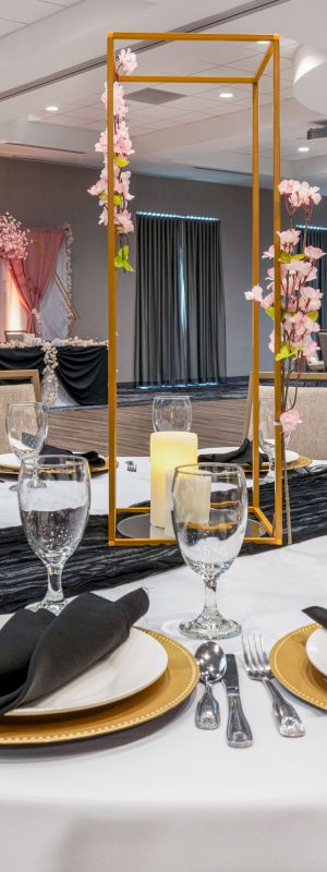 A banquet hall set up for a formal event, with round tables, elegant place settings, black napkins, and decorative centerpieces featuring candles and flowers.