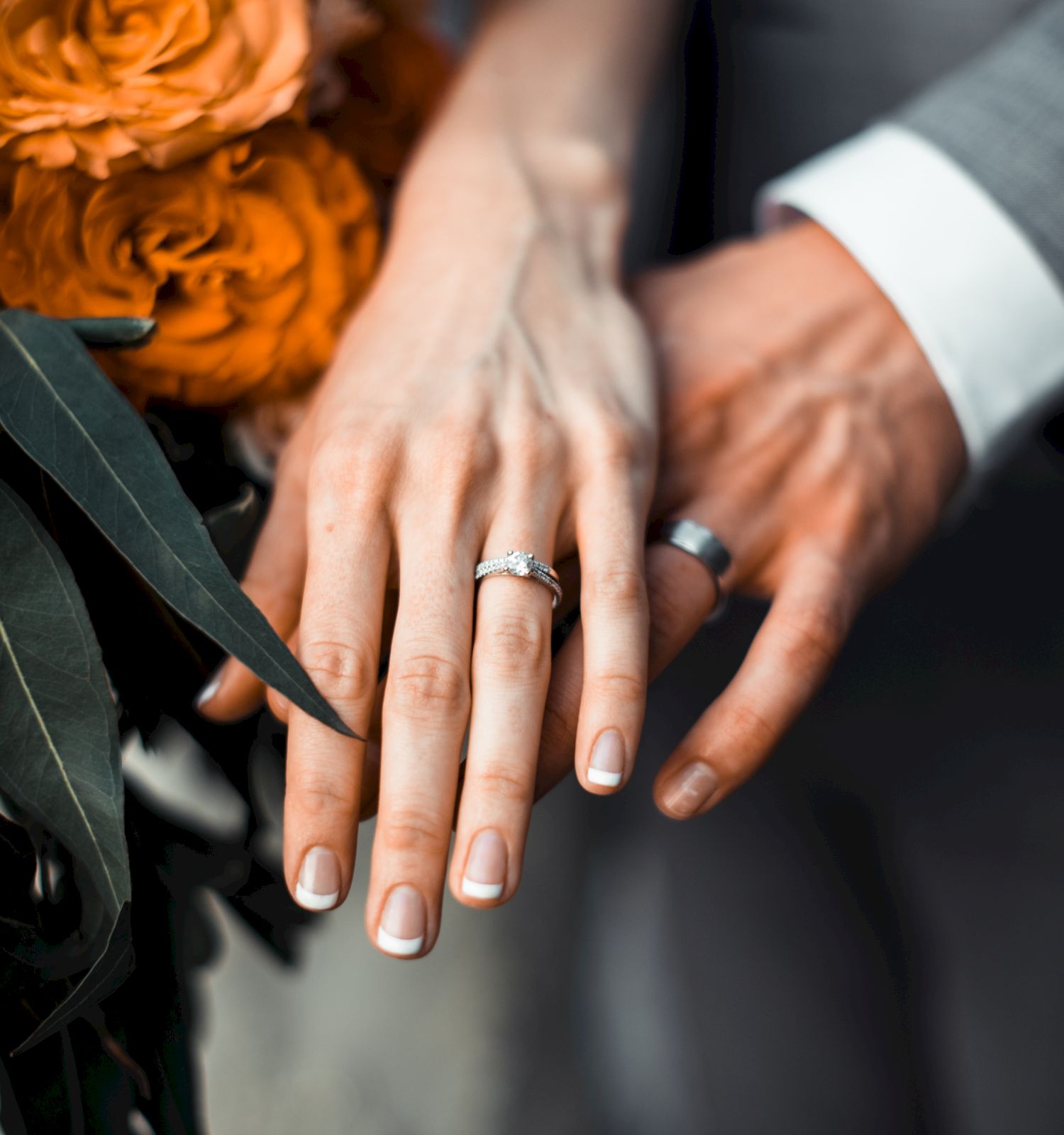 Two hands displaying wedding rings, joined together with flowers in the background. A symbol of love and commitment.
